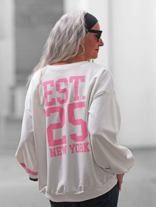Person mit silbernem Haar und Sonnenbrille trägt das OFF#DLY Sweat NY white Sweatshirt, oversized mit pinkem EST. '25 NEW YORK-Druck auf dem Rücken, passend für einen lässigen Streetstyle-Look.