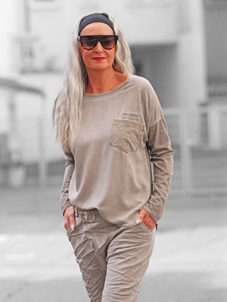 Person trägt OFF#DLY Longsleeve Roma taupe mit lässigem Schnitt und Brusttasche, kombiniert mit passenden Hosen, während sie in einer städtischen Umgebung spazieren geht.