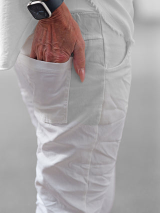 Nahaufnahme einer älteren Hand in der Tasche der OFF#DLY Joggpant Neapel offwhite, die aus weichem, elastischem Stoff mit dekorativer Stickerei besteht und eine bequeme, stilvolle Passform bietet.