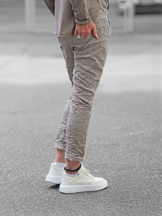 Person trägt OFF#DLY Joggpant Bari grey, eine leichte, knöchellange Jogginghose mit Crinkle-Optik und bequemem Sitz, kombiniert mit weißen Sneakers und einem passenden grauen Oberteil.