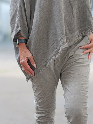 Nahaufnahme des OFF#DLY Shirt Arianna taupe: Locker sitzende, graue Baumwoll-Leinen-Mix-Tunika mit fransigem Saum, getragen mit passender Hose. Eine Hand trägt eine Smartwatch, die andere einen Silberring und hat rosa lackierte Nägel.