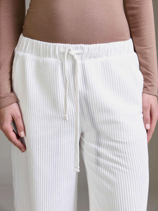 Nahaufnahme einer Person mit Cotton Candy Pant Mehtab offwhite, einer weißen, gerippten Loungehose. Die Hose hat einen elastischen Bund mit Kordelzug und fällt in einem entspannten, weiten Bein.