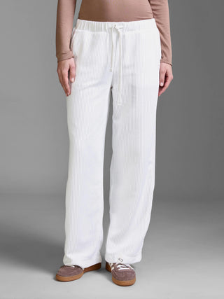 Eine Person trägt die Cotton Candy Pant Mehtab offwhite, eine locker sitzende, elastische Cordhose mit Tunnelzug, geradem Bein und Seitentaschen, kombiniert mit einem langärmeligen Oberteil und Sneakers.