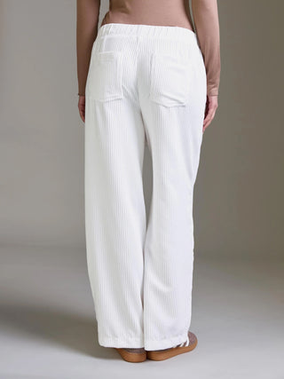 Das Bild zeigt die Cotton Candy Pant Mehtab offwhite mit weitem Bein, elastischem Bund und vertikalen Rippen. Die Hose hat aufgesetzte Gesäßtaschen und wird mit flachen Slip-On-Schuhen kombiniert.