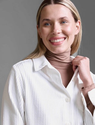 Nahaufnahme einer lächelnden Frau mit der Cotton Candy Jacket Mesude offwhite, einer kurzgeschnittenen, gerippten Cordjacke mit Knopfleiste, über einem taupefarbenen Rollkragenpullover getragen.