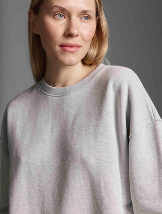 Eine Frau trägt das Cotton Candy Sweatshirt Manon grey melange. Das Sweatshirt hat einen Rundhalsausschnitt, offene Seitennähte und wirkt oversized. Perfekt für einen lässigen, vielseitigen Look.
