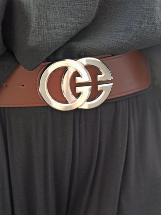 Nahaufnahme eines Taillenbereichs mit dem OFF#DLY Gürtel GG schokobraun/silber, einem braunen Gürtel mit glänzender, doppelter G-Schließe, getragen über einem schwarzen Kleidungsstück.