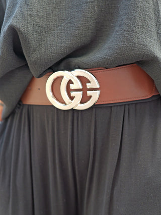 Person trägt OFF#DLY Gürtel GG schokobraun/silber, der eine schwarze, fließende Kleidung an der Taille mit einem glänzenden, silbernen Doppelringverschluss betont. Gürtel in hochwertigem, elastischem Material.