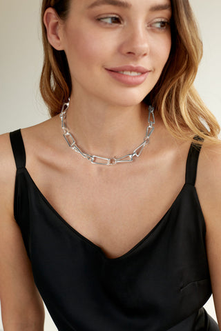 Frau trägt eine OFF#DLY Gliederkette silber mit unregelmäßigen geometrischen Gliedern. Die Kette liegt elegant auf ihrem schwarzen, Spaghetti-Träger-Top. Ihr Kopf ist leicht zur Seite geneigt.