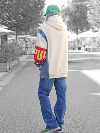 Person von hinten mit dem OFF#DLY Sweatkleid Francesca creme, locker sitzender Hoodie mit auffälligen roten und gelben Prints, kombiniert mit blauer Jeans und grünen Sneakern, auf einer belebten Fußgängerstraße.