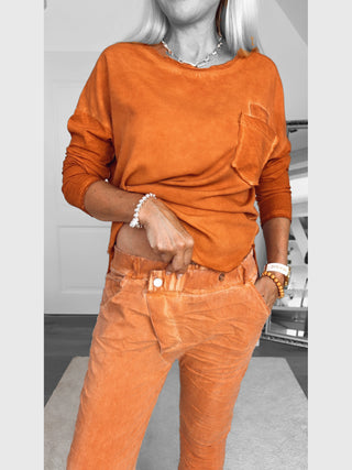 OFF#DLY Joggpant Bari rostorange: Zweiteiliges Loungewear-Set mit langärmligem Pullover und Gummibundhose, ergänzt durch modischen Silberschmuck und Perlenarmbänder, präsentiert in stilvollem, verwaschenem Orange.
