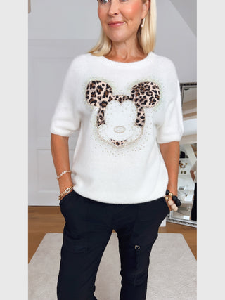 Frau trägt den OFF#DLY Pulli Mickey creme mit großem Mickey-Motiv im Leo-Print und Strassdetails, kombiniert mit schwarzen Cargo-Hosen. Der Pullover vermittelt einen verspielten, gemütlichen Look.