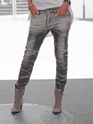 Person trägt OFF#DLY Denim Luino grey Jeans mit schmaler Passform und Used-Effekten, kombiniert mit grauen Stiefeln und einem weißen Oberteil; Armband und Smartwatch sichtbar.