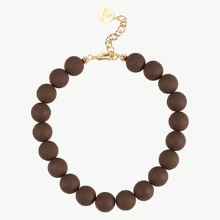 Die OFF#DLY Kugelkette schoko/gold zeigt eine elegante, einsträngige Halskette aus matten, braunen Kugelperlen mit einem goldfarbenen Karabinerverschluss und einer kurzen, verstellbaren Verlängerungskette.