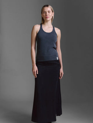 Frau in einem Cotton Candy Tank Top Lois black mit gekreuzten Trägern und figurbetonter Passform, kombiniert mit einem langen schwarzen Rock, präsentiert das Top in einem schlichten Studio-Setting.