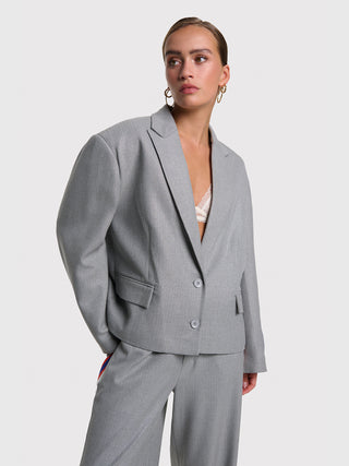 Junge Frau trägt den ALIX Coated Blazer soft grey melange mit breitem Fischgrätenmuster, kombiniert mit passenden weiten Hosen. Der Blazer hat eine Oversize-Passform und Fronttaschen.