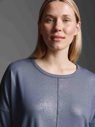 Nahaufnahme einer jungen Frau mit glattem, schulterlangem Haar, die das Cotton Candy Tee Margaux blue ash trägt. Das gerippte, glitzernde Langarmshirt hat einen Rundhalsausschnitt und eine überschnittene Schulter.