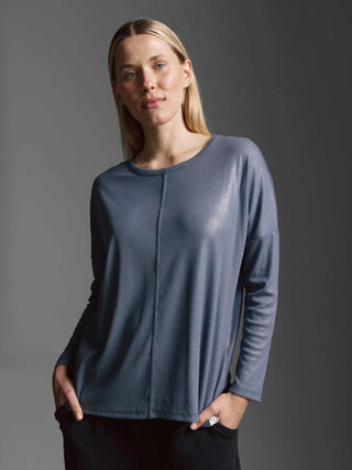 Frau trägt das Cotton Candy Tee Margaux blue ash, ein oversized, geripptes Langarmshirt mit Rundhalsausschnitt und überschnittener Schulter, kombiniert mit schwarzen Hosen.