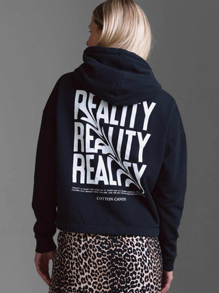 Person von hinten in einem schwarzen Cotton Candy Sweatshirt Malve mit Kapuze, bedruckt mit dem Wort REALITY und motivierender Textbotschaft, kombiniert mit einem Leopardenrock.