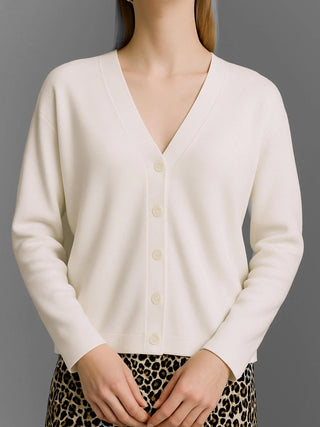 Eine Person trägt den Cotton Candy Cardigan Ori white, einen oversized, cremefarbenen V-Ausschnitt-Cardigan mit Knopfleiste, kombiniert mit einem Leopardenmuster-Rock oder -Hose.