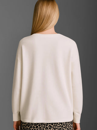 Die Rückansicht einer Frau in einem Cotton Candy Cardigan Ori white, locker sitzend mit überschnittener Schulter und gerippten Bündchen, kombiniert mit einem Leopardenmuster-Rock oder -Hose.