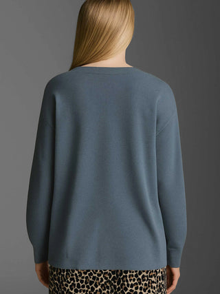 Rückansicht eines Modells mit langem, blondem Haar, das den Cotton Candy Cardigan Ori blue ash trägt, einen oversized, langärmligen Strick-Cardigan mit Knopfleiste, kombiniert mit einem Leopardenrock.