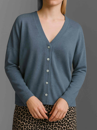 Person trägt Cotton Candy Cardigan Ori blue ash, ein V-Ausschnitt-Cardigan mit Knopfleiste, langen Ärmeln und überschnittener Schulter. Darunter ein Rock oder Kleid mit Leopardenmuster.