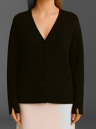 Das Cotton Candy Cardigan Kristi black ist ein schwarzer, oversized Strickcardigan mit V-Ausschnitt, drei Knöpfen, langen Ärmeln und Daumenschlitzen, getragen über einem hellen Rock.