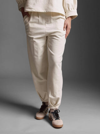 Person trägt die Cotton Candy Pant Giana offwhite, eine oversized geschnittene, gewaschene Sweatpants mit elastischen Bündchen und seitlichen Taschen, die entspannt mit Händen in den Taschen präsentiert wird.