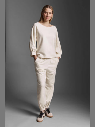 Frau trägt Cotton Candy Pant Giana offwhite, eine oversized, gewaschene Sweatpants mit seitlichen Taschen und besonderem Beinsaum, kombiniert mit einem passenden langärmligen Oberteil und rosa Sneakers.