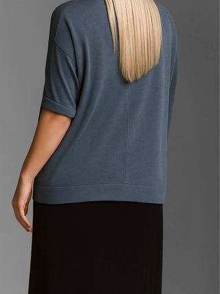 Person von hinten in lockerem, schieferblauem T-Shirt mit Ellenbogenärmeln und geradem schwarzen Rock. Das T-Shirt ist das Cotton Candy Tee Helay black melange mit sichtbaren Saumnähten.