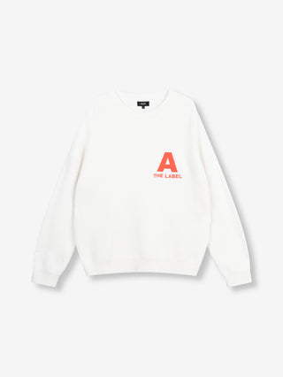Der ALIX Basic Jumper cream zeigt einen weißen, langärmeligen Waffelstrick-Pullover mit rotem „A“ und „THE LABEL“ auf der Brust, lockerem Sitz und Rundhalsausschnitt.