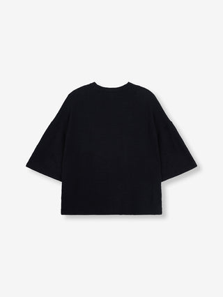 ALIX Boucle Tee black aus Bouclé-Jersey mit weitem, übergroßem Schnitt, Rundhalsausschnitt, kurzen Ärmeln, und „THE LABEL”-Stickerei auf der Brust, flach auf weißem Hintergrund präsentiert.
