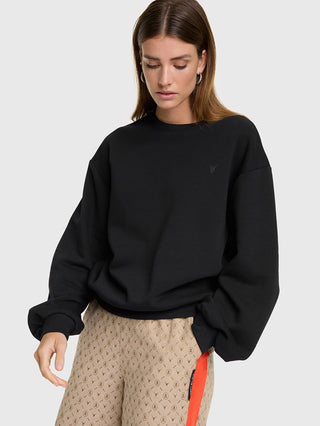 Eine Person trägt einen ALIX Photoprint Sweater black mit leicht übergroßem Schnitt, gerippten Bündchen und rundem Halsausschnitt. Kombiniert mit hochtaillierten, beige bedruckten Hosen und einem roten Streifen.
