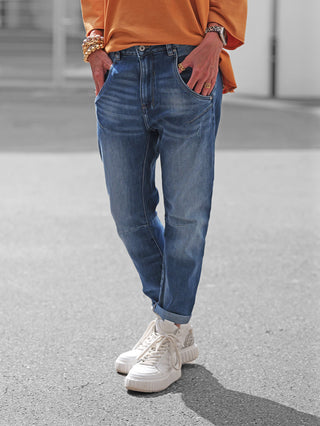 Die OFF#DLY Denim Parma lightblue zeigt sich als moderne Jeans mit umgeschlagenem Saum, kombiniert mit lässigen Sneakern und goldfarbenem Schmuck für einen stilvollen, urbanen Street-Style-Look.