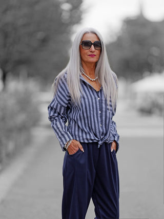 Ältere Frau auf Straße in OFF#DLY Bluse Eva blue, vertikal gestreift und geknotet, mit Perlenkette, Armbandstapel und Oversized-Sonnenbrille, vermittelt einen lässigen, modischen Look.