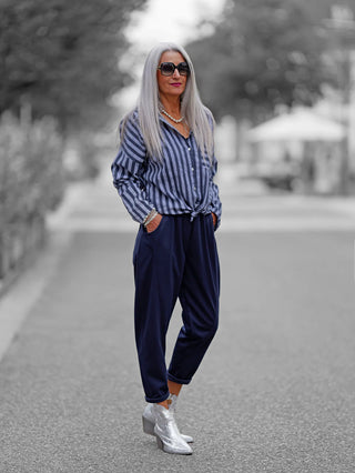 Frau trägt die OFF#DLY Bluse Eva blue, eine blau-weiß gestreifte Bluse mit Knopfleiste und Brusttasche, kombiniert mit lockeren navy Hosen und silbernen Stiefeletten.