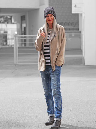 Frau trägt die OFF#DLY Sweatjacke Hope taupe, mit Kapuze und Fronttaschen, über gestreiftem T-Shirt und Jeans. Die Jacke ist lässig und bequem, ideal für urbanen Stil.