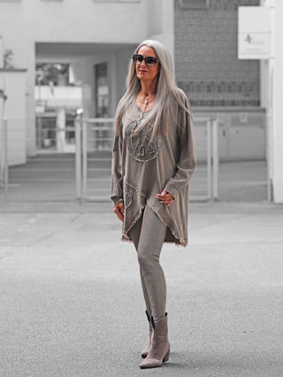 Frau trägt OFF#DLY Snake Legging taupe, eng anliegend und glänzend, kombiniert mit einer langen Tunika. Komplettiert mit goldener Halskette und roten Lippen im urbanen Umfeld.