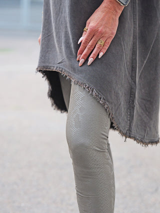 Person trägt OFF#DLY Snake Legging taupe, schmal geschnitten, mit Schlangenmuster in gedämpftem Grau, kombiniert mit einem dunkelgrauen, ausgefransten Tunika-Top. Die Hand zeigt rosa Nägel, Goldringe und eine Uhr.