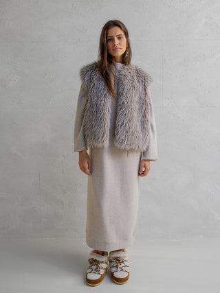 Frau trägt eine Penn&Ink Weste grey aus weichem Stoff über einem beigen Kleid. Die Weste verleiht dem minimalistischen Winter-Look mit ihrem luxuriösen und warmen Design einen Hauch von Glamour.