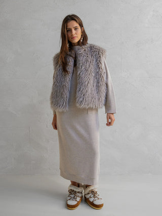 Frau trägt eine Penn&Ink Weste grey über einem langärmeligen, knöchellangen Strickkleid. Die Weste aus weichem, grauem Kunstfell verleiht dem Outfit einen Hauch von Glamour.