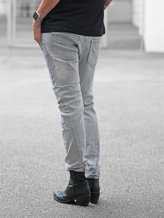 Person trägt OFF#DLY Denim Sergnano grey Jeans, hellgrau mit Used-Effekten, eng anliegend, umgeschlagen am Knöchel. Kombiniert mit schwarzen Western-Stiefeletten und einer Smartwatch mit Leopardenband.