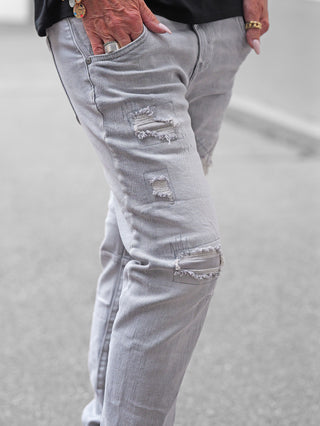 OFF#DLY Denim Sergnano grey Jeans, hellgraue Jeans mit zerstörten Details an Oberschenkel und Knie, rechte Hand mit Schmuck in Fronttasche, betont urbanen, lässigen Look und hochwertigen Materialmix.