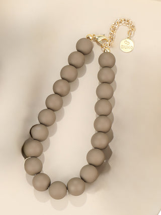 Einzelne OFF#DLY Kugelkette taupe/gold aus matten, taupefarbenen Perlen mit goldfarbener Verlängerungskette und Karabinerverschluss, geprägt mit GIUNO auf einem kleinen Anhänger.