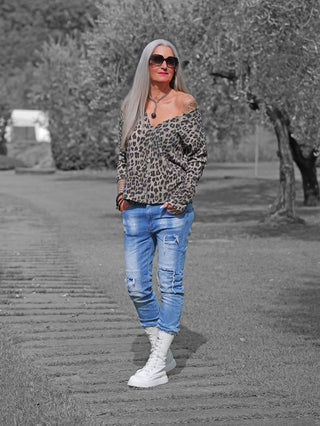 Frau trägt OFF#DLY Jacke Linnea Leo green black mit modernem Leo-Print, lockerem Schnitt und offener Schulterpartie. Kombiniert mit blauer Jeans und weißen Stiefeln, präsentiert sie einen lässigen, stilvollen Look.