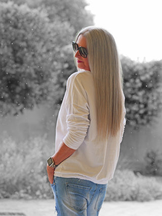 Frau von hinten in OFF#DLY Shirt Smile white, locker sitzend, lange Ärmel, mit Rundhalsausschnitt. Kombiniert mit blauen Jeans und einer Uhr, vermittelt sie einen lässigen, entspannten Look.