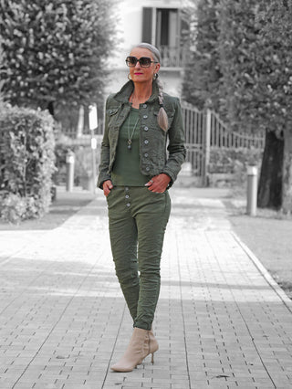 Eine Frau trägt OFF#DLY Color Jeans Imelda khaki in schlankem Schnitt, kombiniert mit einem passenden olive-grünen Outfit, das ihre Figur betont und Bewegungsfreiheit bietet.