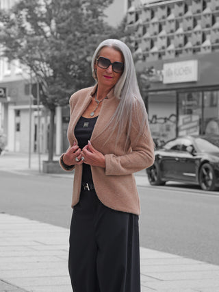 Eine stilvolle Frau trägt den OFF#DLY Blazer Sibilla camel. Der taillierte Blazer mit Stehkragen verleiht ihr eine elegante Silhouette, ideal für vielseitige Kombinationen.