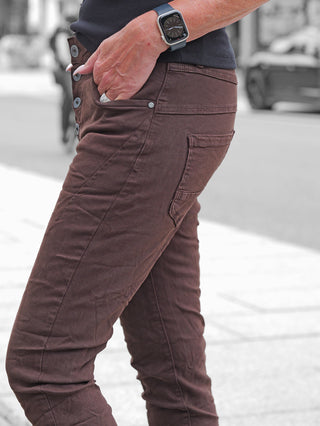 Nahaufnahme einer Person, die die OFF#DLY Color Jeans Imelda schoko trägt. Die schlanke Passform betont die Figur, während eine Hand in der Tasche einen silbernen Ring zeigt.